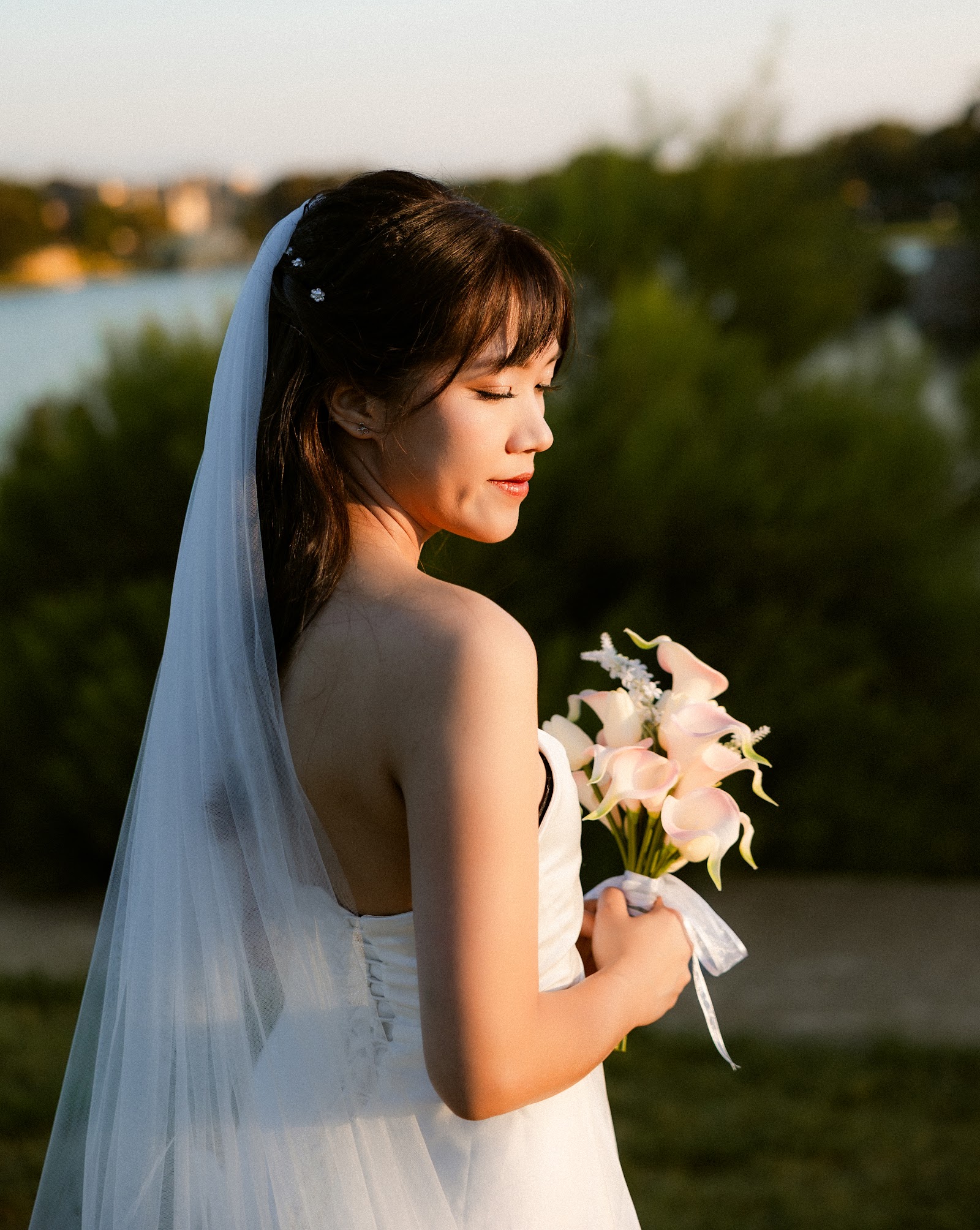 A bride in a flowing veil holding white flowers against the evening sky