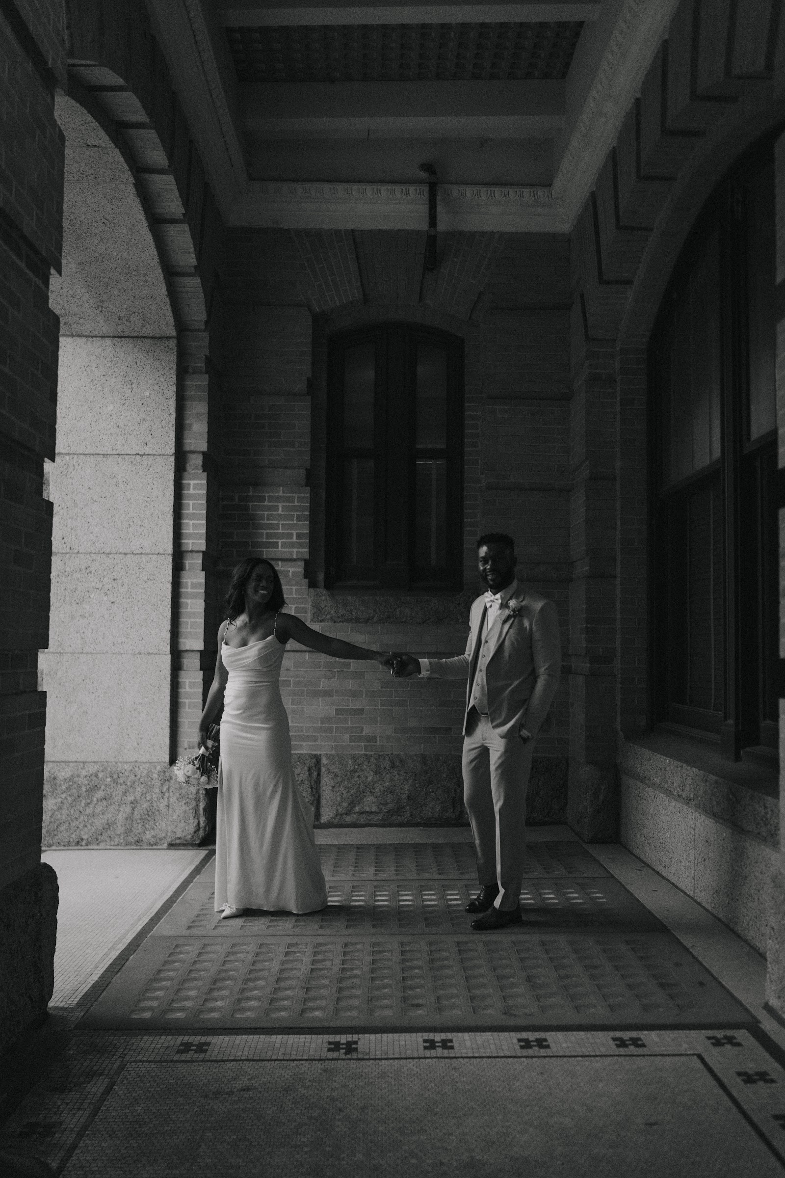 A bride and groom meeting beneath a stone archway in black and white