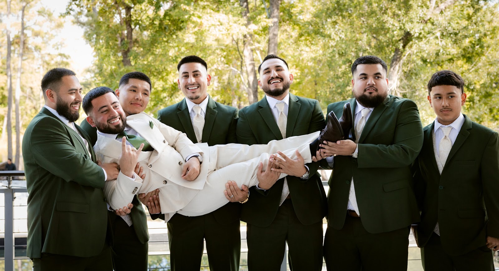 Groomsmen lifting the groom in celebration on the lawn