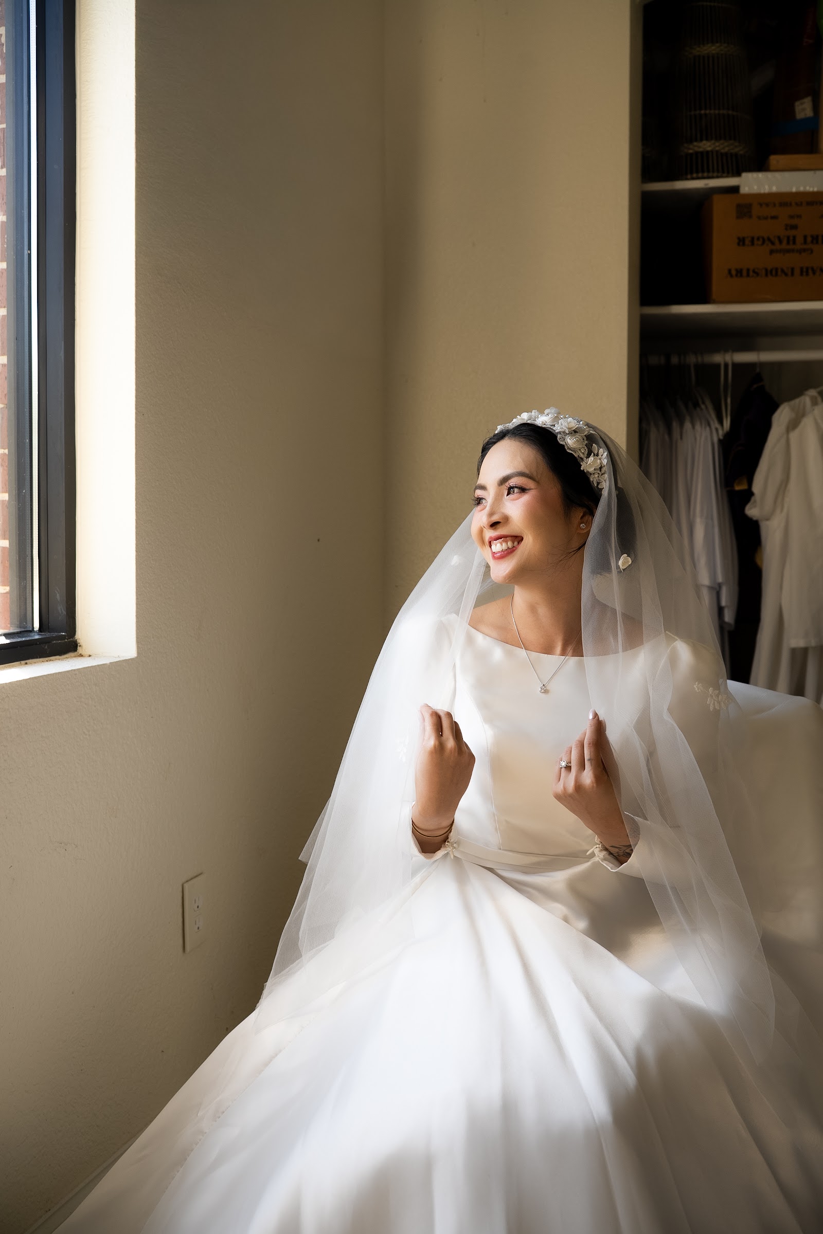 A bride laughing softly beside a tall window as morning light fills the room