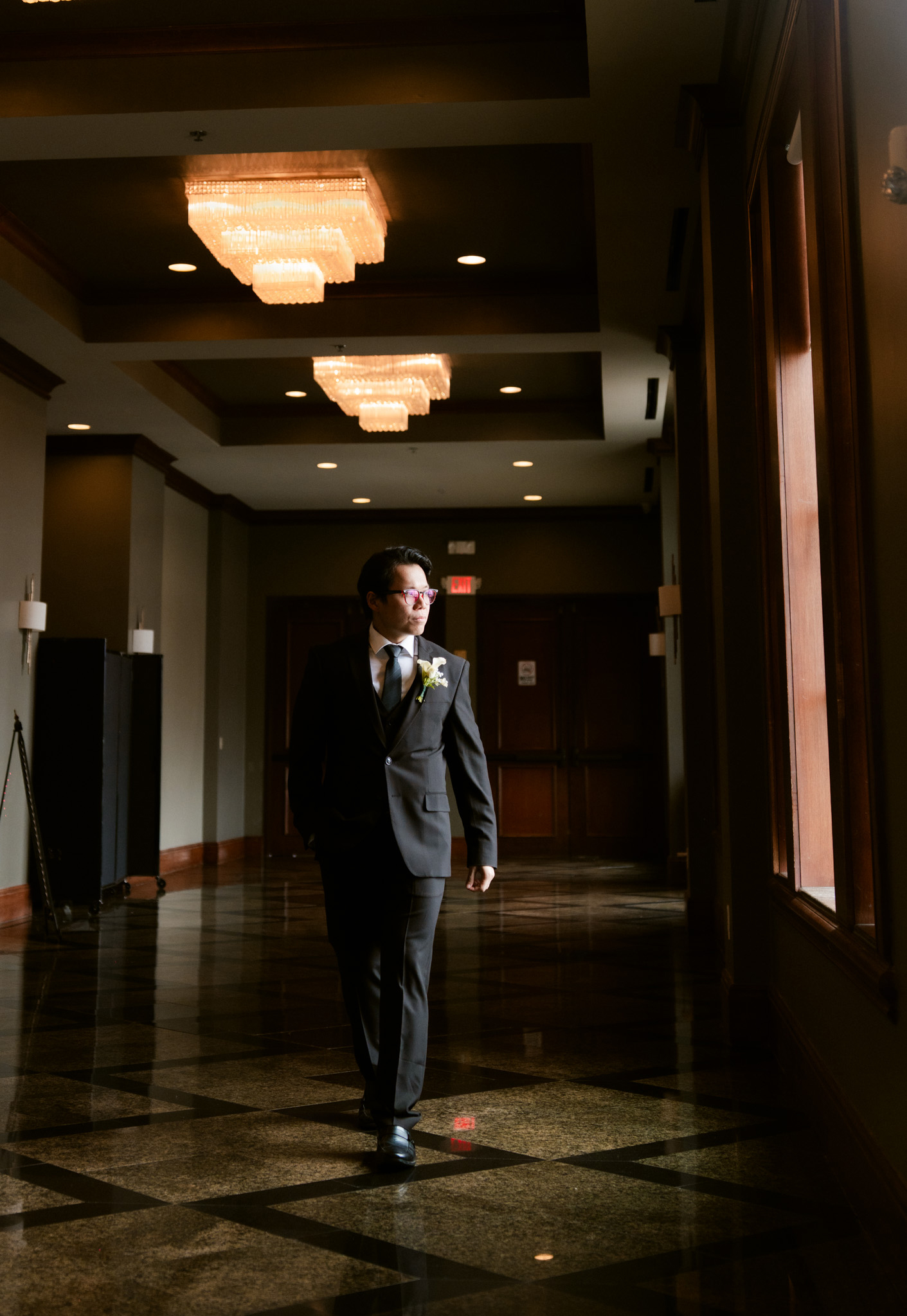 A groom walking a grand hallway alone, light falling across the marble floor
