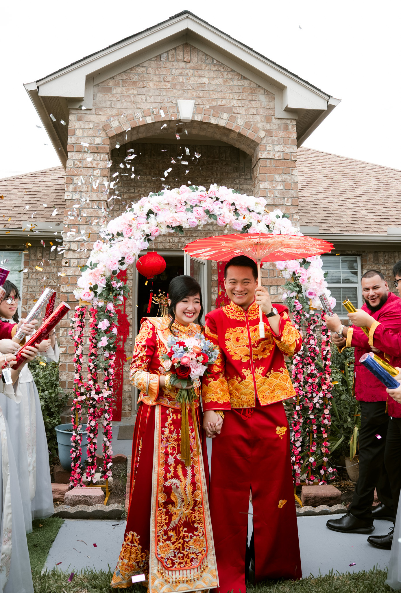 Yida and Sherri walking hand in hand through a red-curtained gateway with their families