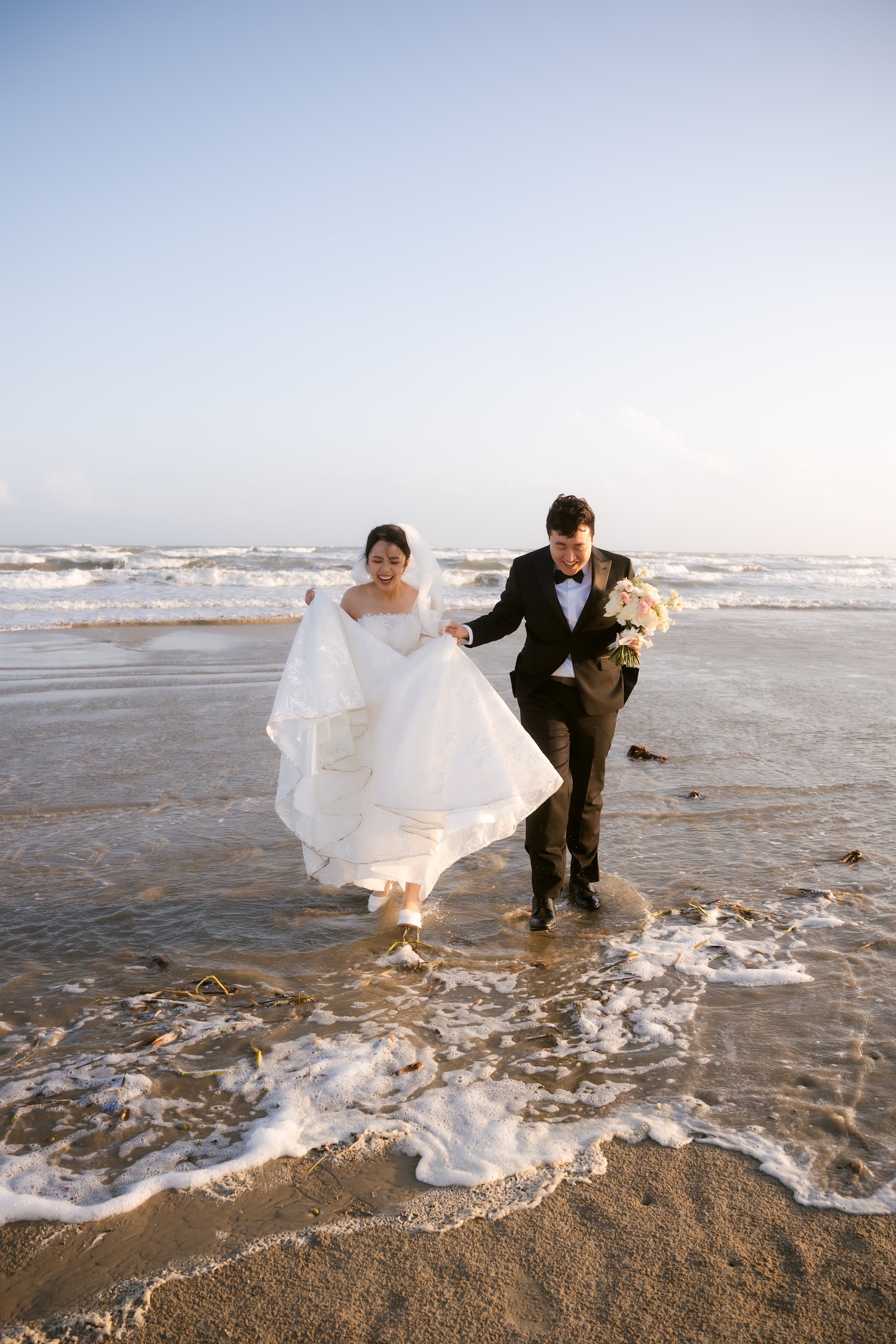 A couple embraced by a rushing wave at the water's edge