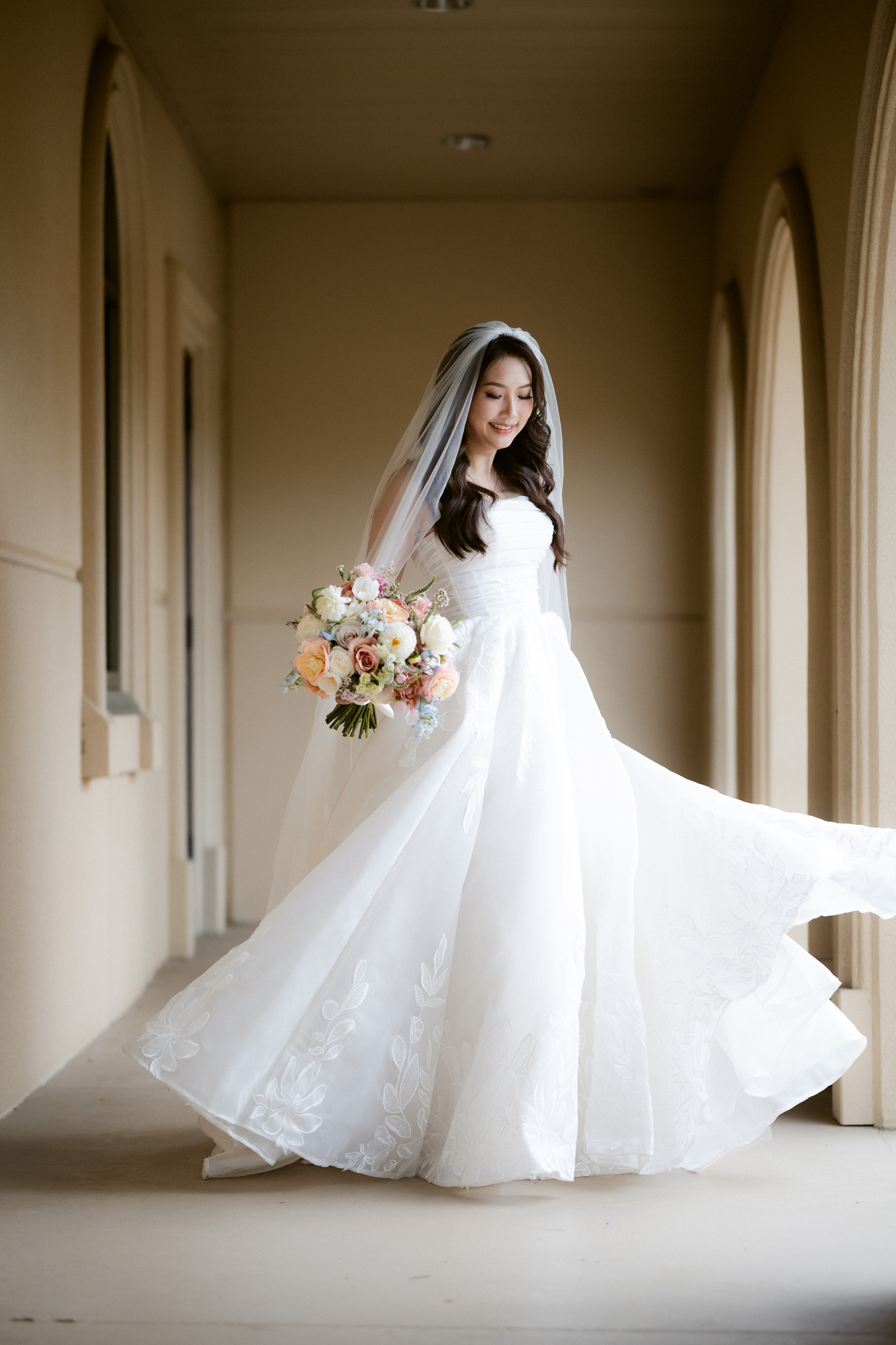 A bride standing in a sunlit corridor, her long veil falling toward the floor