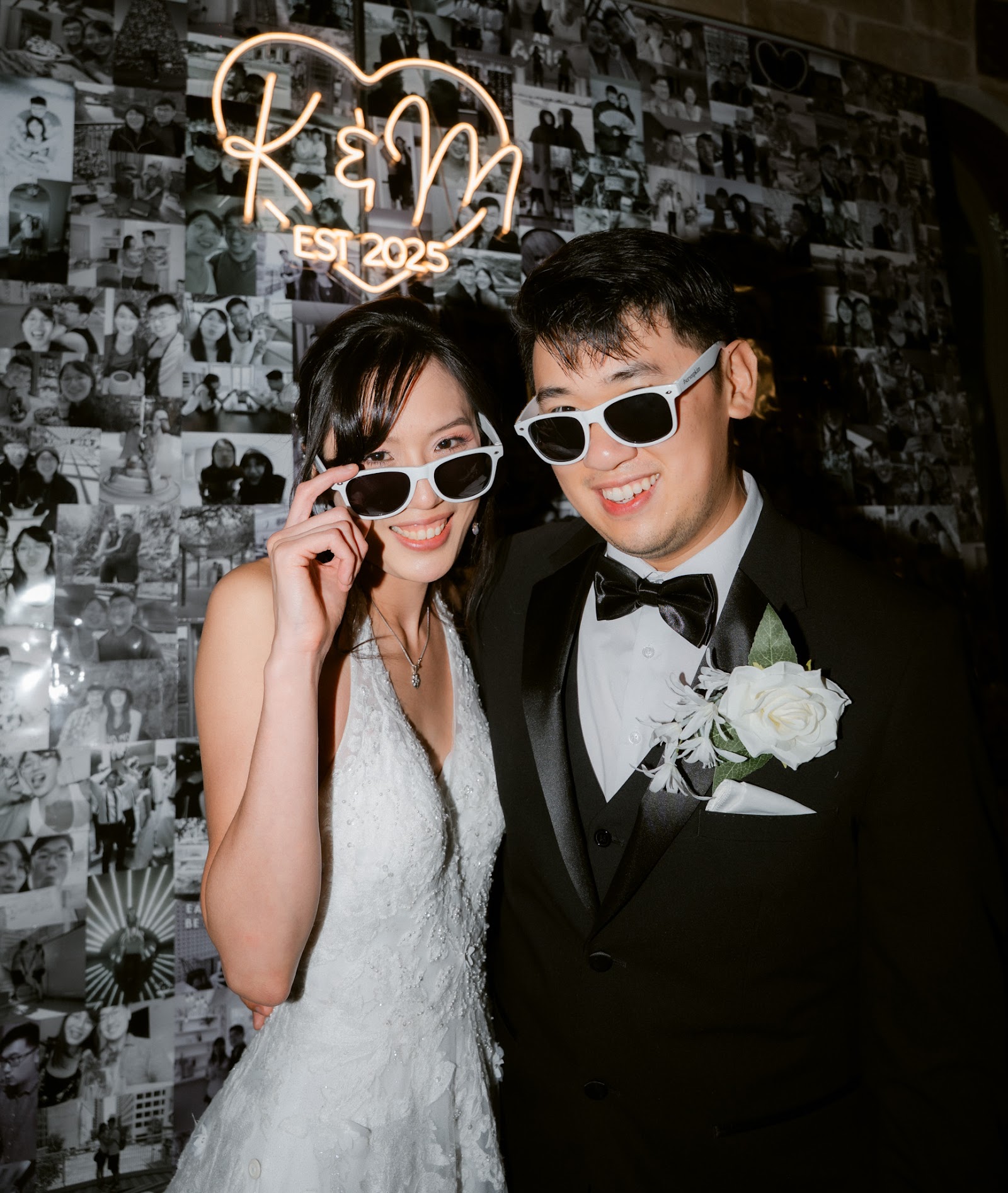 A couple in sunglasses posing playfully beneath a neon sign